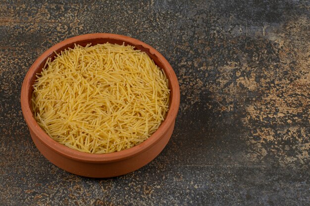 Bowl of raw macaroni on marble surface. 