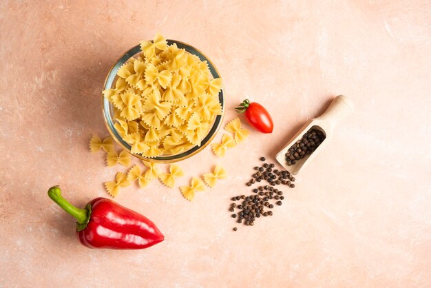 Bowl of raw pasta and fresh vegetables on orange.