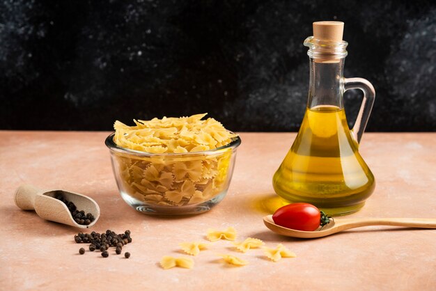 Bowl of raw pasta and olive oil on orange table.