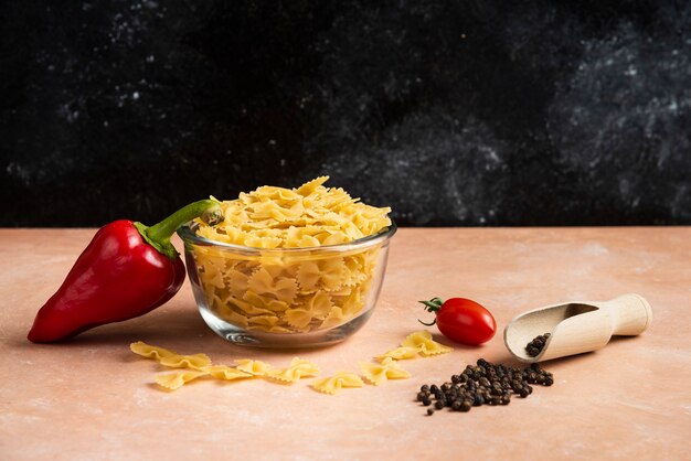 Bowl of raw pasta, pepper grains and fresh vegetables on orange.