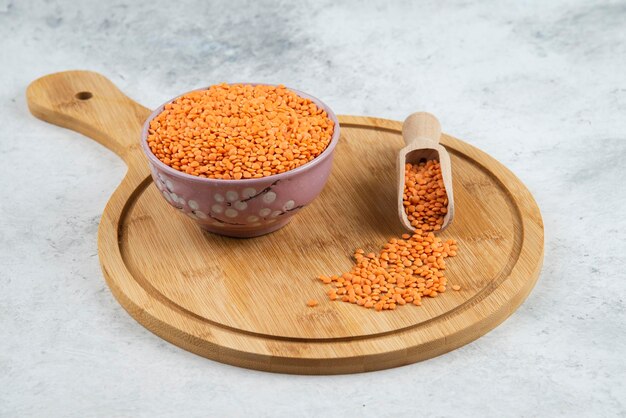 Bowl of raw red lentils and spoon on cutting board.