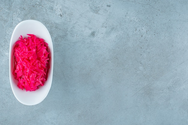 A bowl of red fermented sauerkraut, on the blue table. 