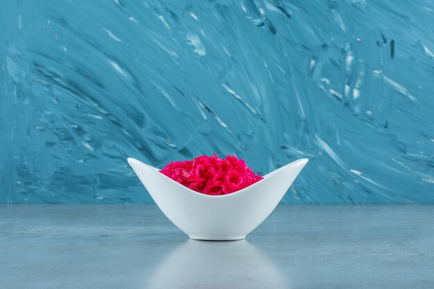 A bowl of red fermented sauerkraut, on the blue table. 