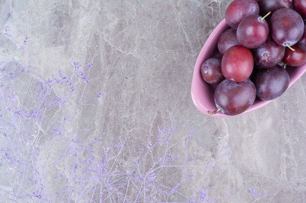 Free photo bowl of ripe plums on stone background.