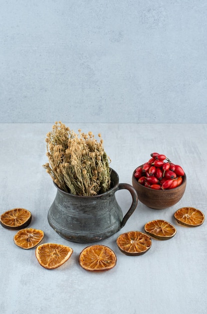 Free photo bowl of rosehips, dried orange and rue on stone surface.