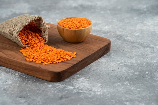 Free photo bowl and sackcloth of red raw lentils on wooden board.