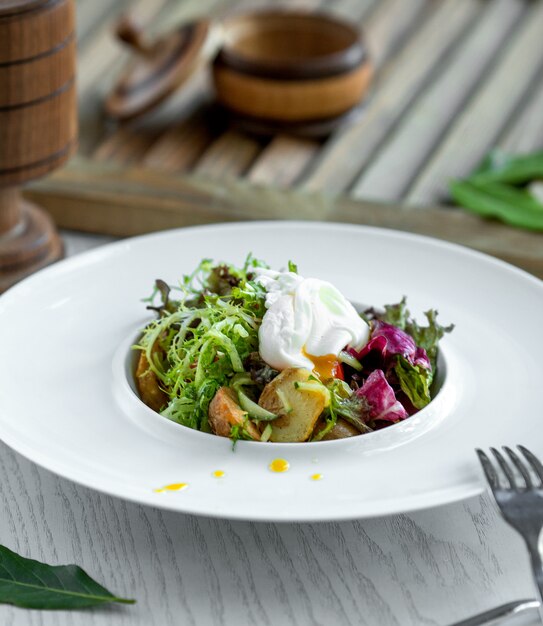 Bowl of salad with fried potatoes, arugula, cucumber, lettuce and yoghurt