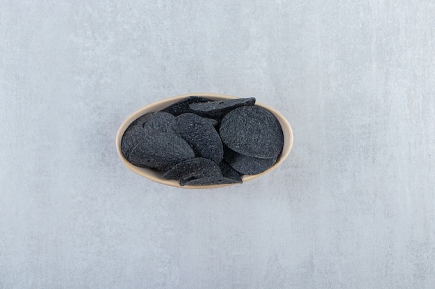 Bowl of salted crispy black chips on stone.