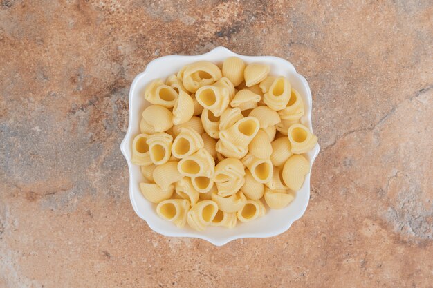 Bowl of seashell shaped pasta on marble background