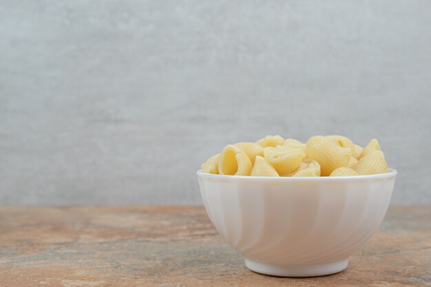 Bowl of seashell shaped pasta on marble background