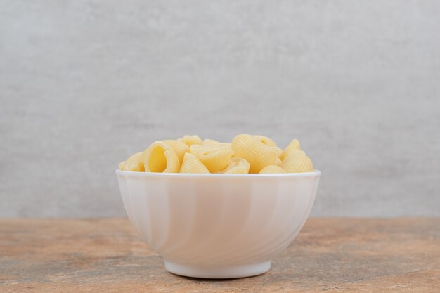 Bowl of seashell shaped pasta on marble background