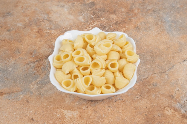 Free photo bowl of seashell shaped pasta on marble space.