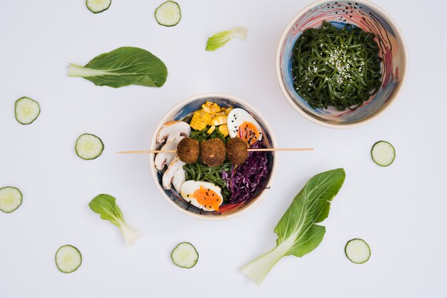 Чаша салат из морских водорослей с рамен традиционной азиатской кухни, украшенные ломтиками огурца и листьев на белом фоне