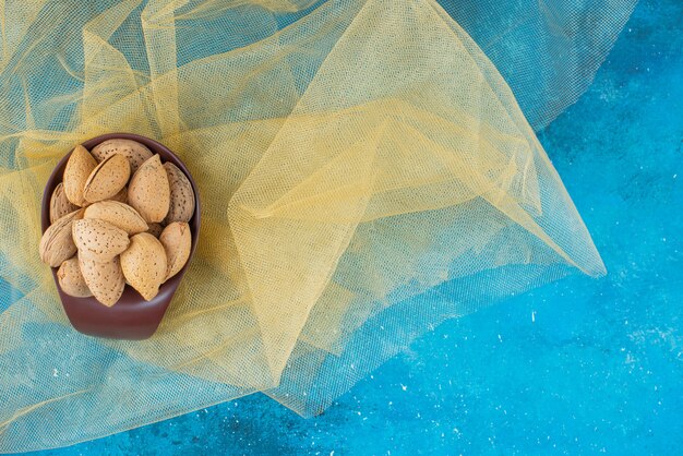 A bowl of shelled almonds on tulle , on the blue table. 