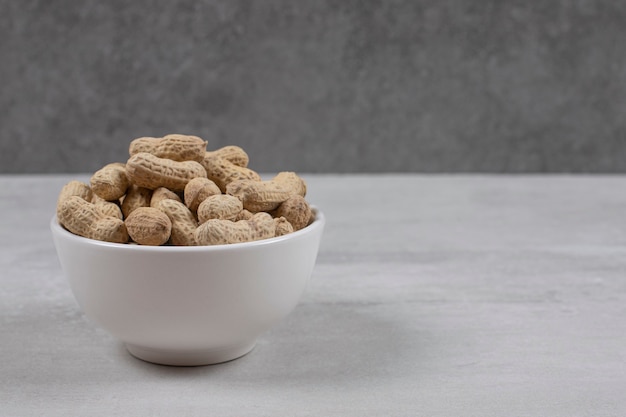 Bowl of shelled peanuts on marble background.