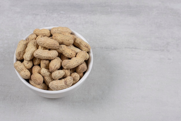 Bowl of shelled peanuts on marble background.