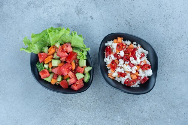 Bowl of shepherd's salad next to a bowl of pepper and cauliflower salad on marble surface