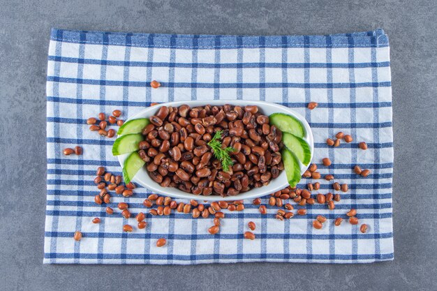 Bowl of sliced cucumber and beans on a towel on the marble surface