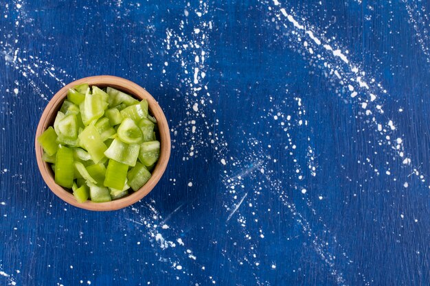 Bowl of sliced green bell peppers on marble table.