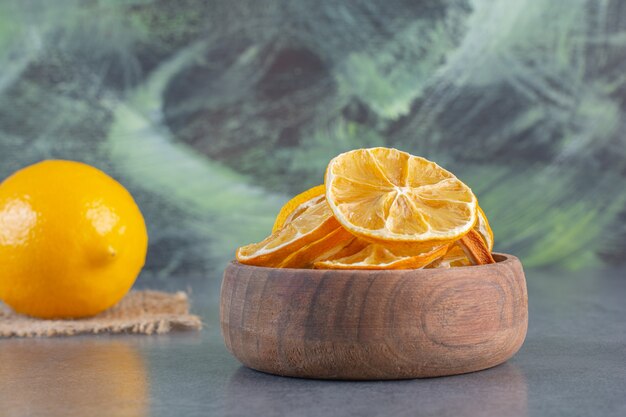 Bowl of sliced lemons and whole lemon on stone background.