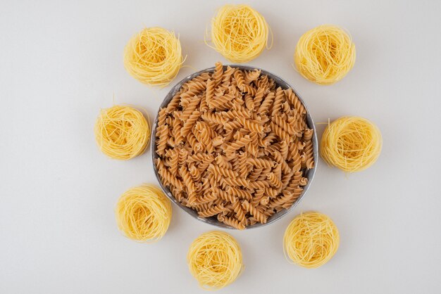 Bowl of spiral pasta and spaghetti nests on white surface