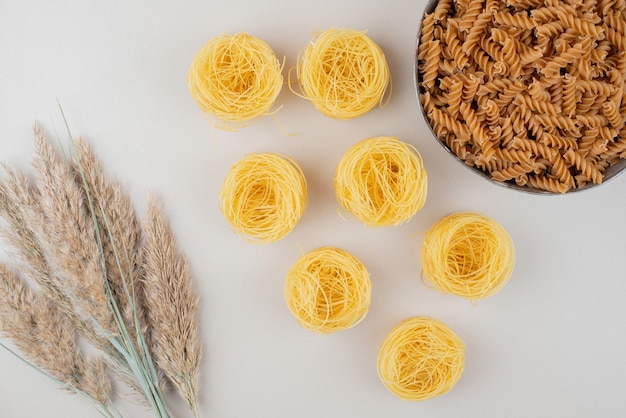 Bowl of spiral pasta and spaghetti nests on white surface