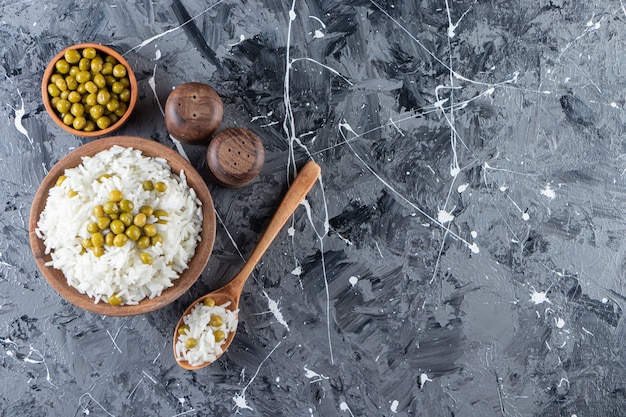 Bowl of steamed white rice with green peas on marble background. 