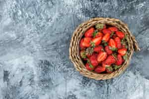 Free photo a bowl of strawberries on a wicker placemat on a dark blue marble background. top view. free space for your text