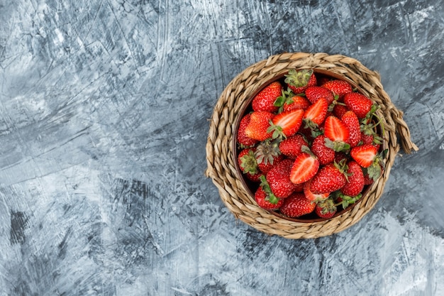 A bowl of strawberries on a wicker placemat on a dark blue marble background. top view. free space for your text