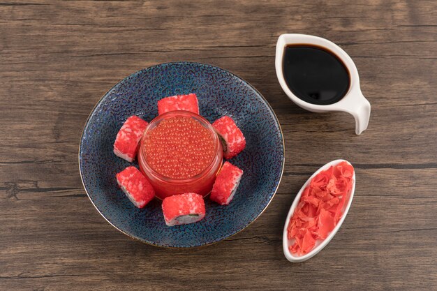 스시 롤과 간장과 생강 나무 테이블에 빨간 캐 비어의 그릇