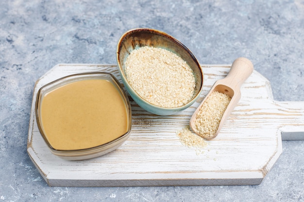 Bowl of tahini with sesame seeds on concrete surface