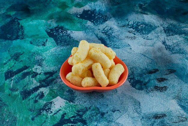 A bowl of tasty corn sticks , on the blue table.