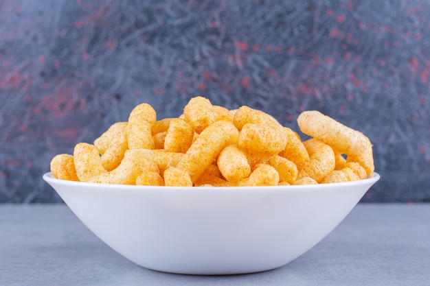 A bowl of tasty corn sticks on marble.