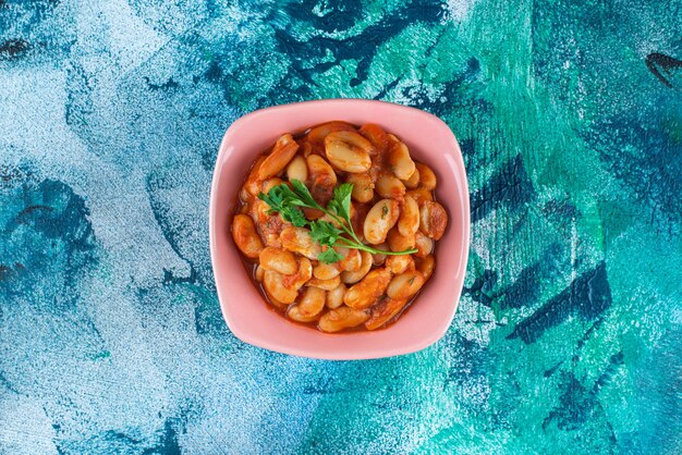 A bowl of toothsome baked beans, on the blue table. 