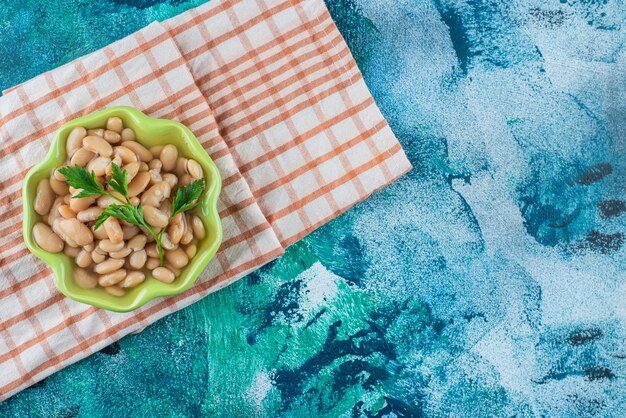 A bowl of toothsome baked beans on a tea towel, on the blue background. 