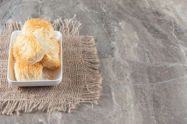 A bowl of Turkish dessert kadayif on a texture on blue.