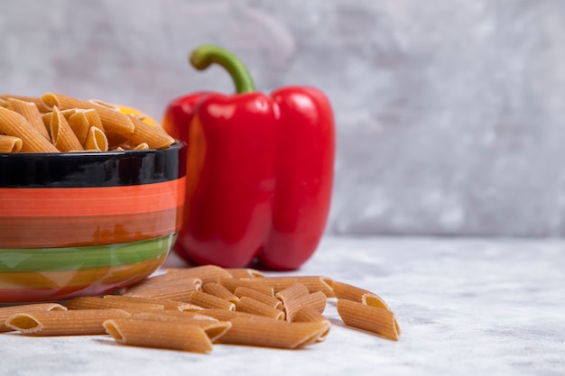 A bowl of uncooked tube pasta with red bell pepper