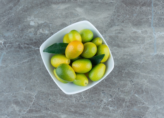 Free photo a bowl of unripe kumquat , on the marble table.