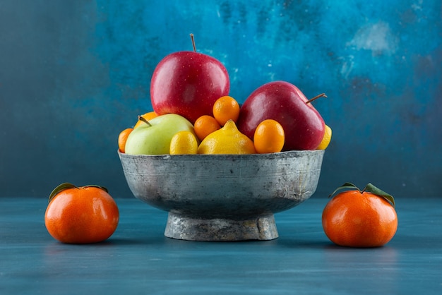 Bowl of various fresh fruits placed on blue surface.