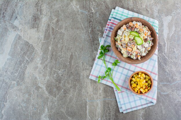 大理石のティータオルのボウルにコーンサラダの隣に野菜サラダのボウル。