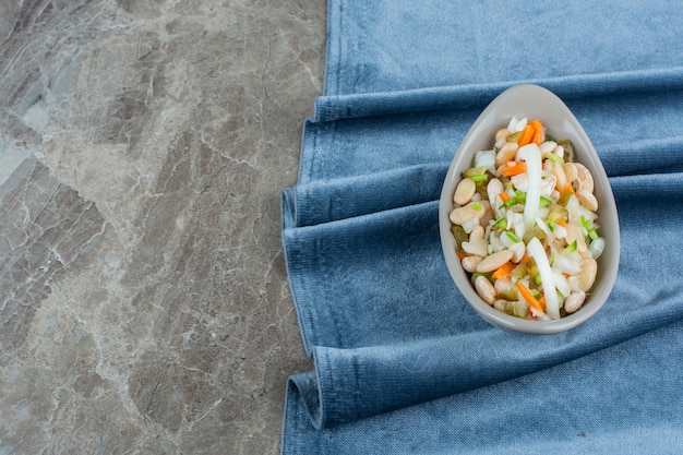 Una ciotola di insalata di verdure su pezzi di tessuto su marmo.