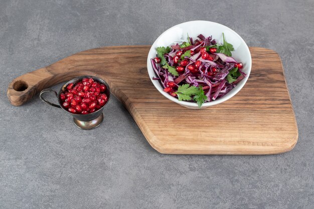 Bowl of vegetable salad on wooden board with pomegranate seeds. High quality photo