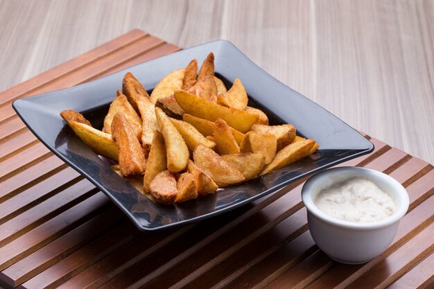 Bowl of village fries and a small bowl of sauce on a wooden table