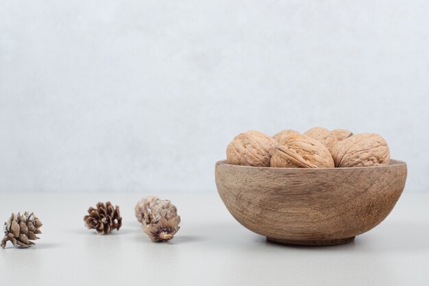 Bowl of walnuts and pinecones on beige surface