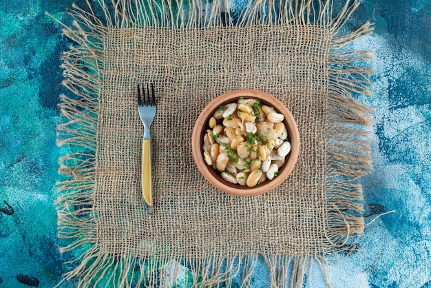 Una ciotola di fagioli bianchi accanto alla forchetta su una trama, sul tavolo blu.