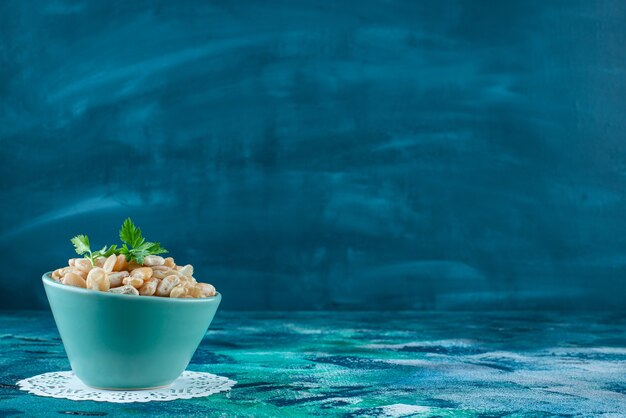 A bowl of white beans with parsley , on the blue table. 