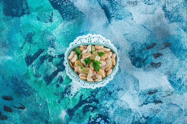 A bowl of white beans with parsley , on the blue table. 