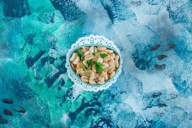 A bowl of white beans with parsley , on the blue table. 