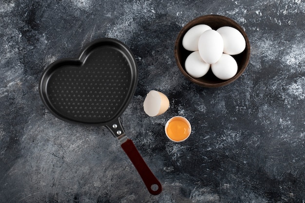 Free photo bowl of white eggs and yolk next to heart shaped pan.