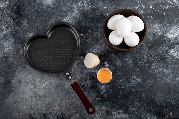 Bowl of white eggs and yolk next to heart shaped pan. 